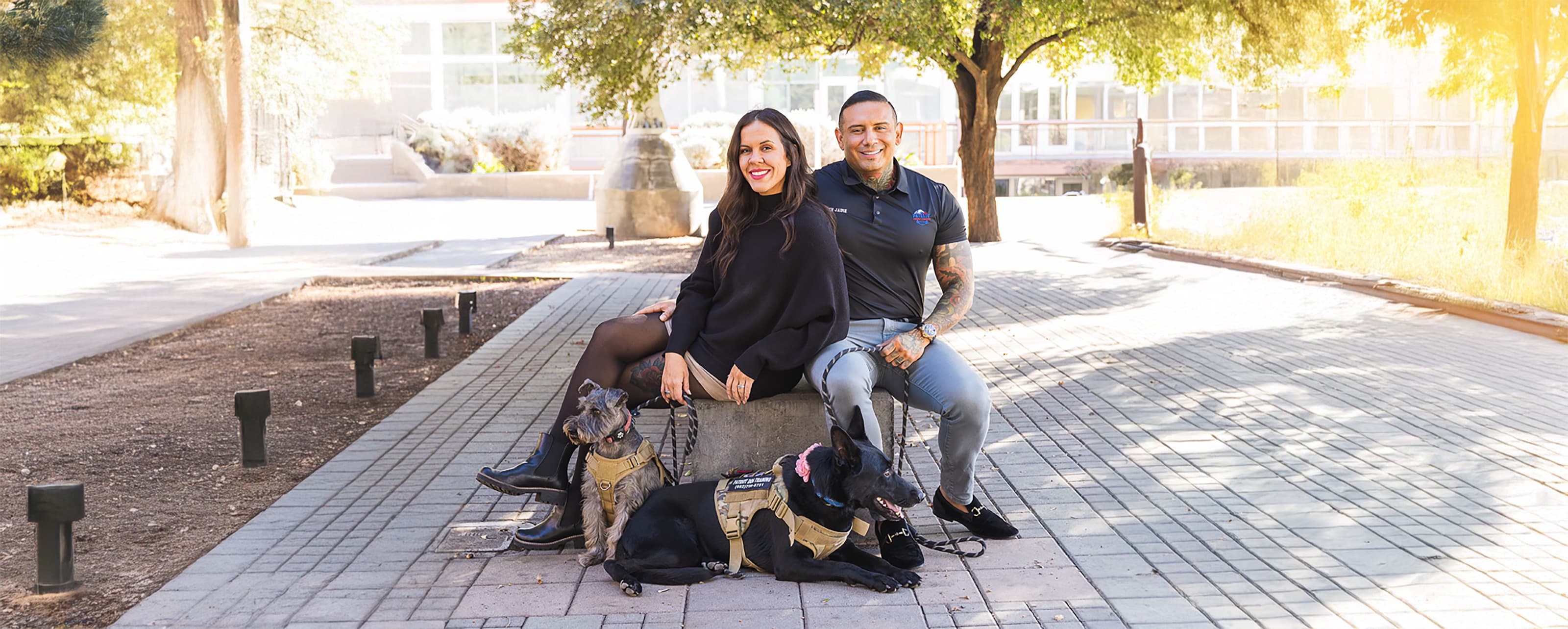 Sydney and Jaime Martinez seated outdoors in warm sunlight with their two dogs
